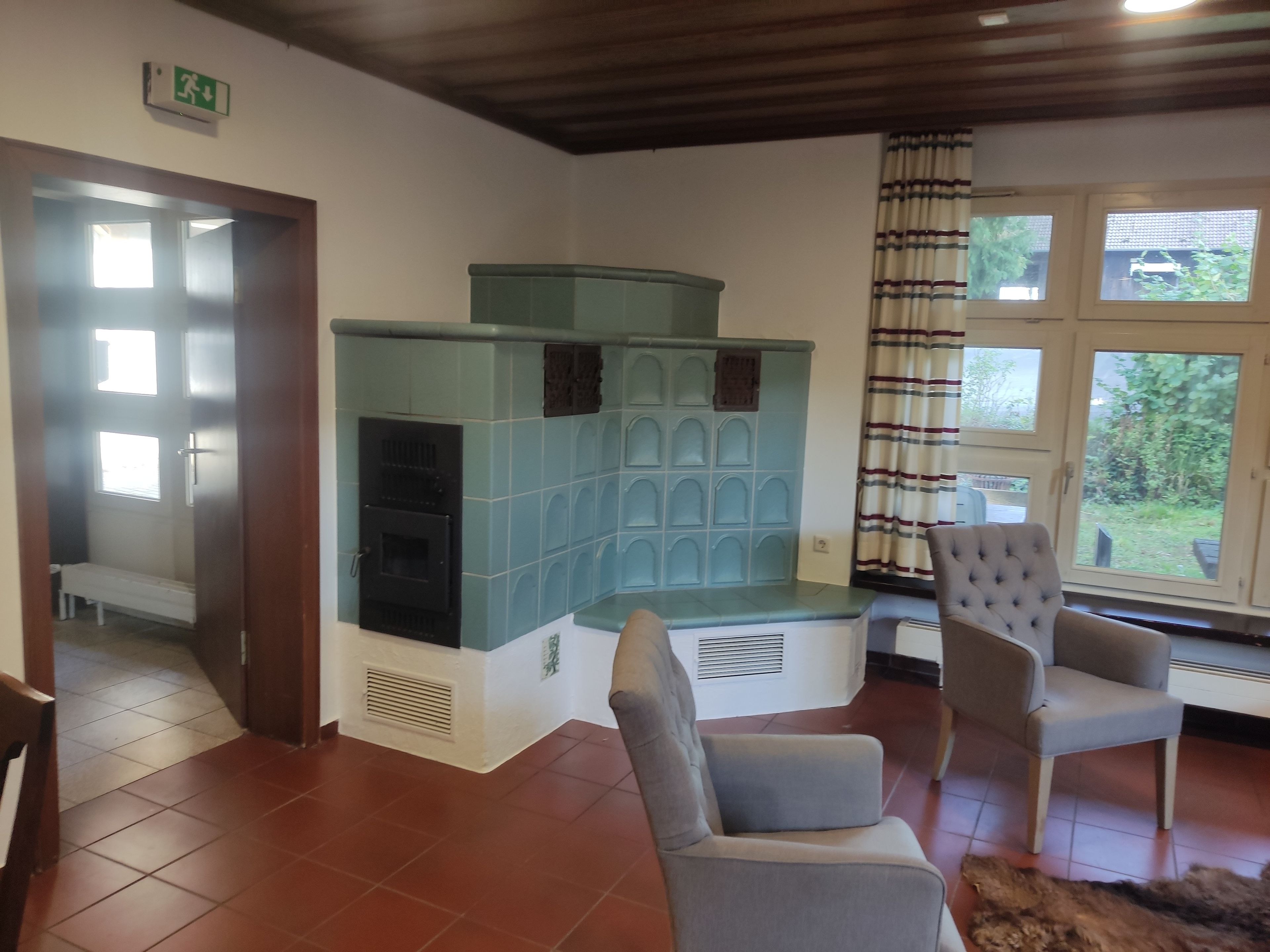 Ein Zimmer mit Kamin, einer Bank, einem Sessel und Blick ins Freie durch ein Fenster.