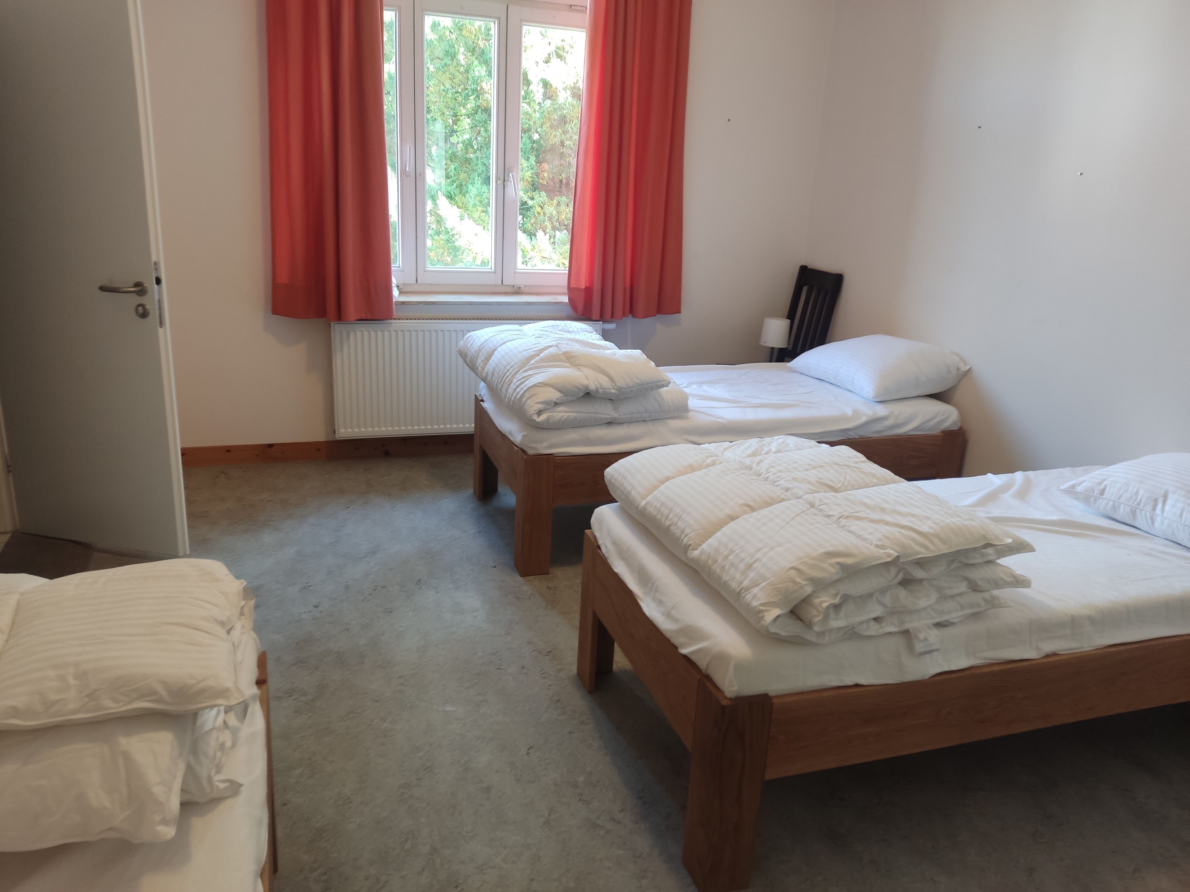 A room with two wooden beds, a radiator, a window with curtains, and a door.