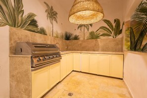 A kitchen with a built-in gas stove, yellow cabinets, and a woven light fixture. - Beautiful 13 BR House in the Old City (Cartagena de Indias)