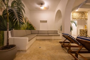 A modern interior with a beige sectional sofa, a wooden lounge chair, and a large potted plant. - Beautiful 13 BR House in the Old City (Cartagena de Indias)