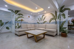 A modern living room with a sectional sofa, a wooden coffee table, and a wall mural with tropical plants and a mountain landscape. - Beautiful 13 BR House in the Old City (Cartagena de Indias)