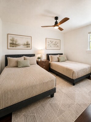 Une chambre avec deux lits, un ventilateur de plafond et des œuvres d’art accrochées aux murs.