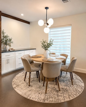 A modern dining area with a round table, four chairs, a vase with plants, and a ceiling light fixture. - Fully Furnished 3BR + Bonus Room, Golf Course, Horseshoe Bay (Horseshoe Bay)