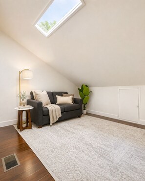 A room with a sloped ceiling, a sofa, a small side table, a floor lamp, a potted plant, and a radiator. - Fully Furnished 3BR + Bonus Room, Golf Course, Horseshoe Bay (Horseshoe Bay)