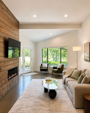 A modern living room with a fireplace, a sofa, a coffee table, and a TV mounted on a wooden wall. - Fully Furnished 3BR + Bonus Room, Golf Course, Horseshoe Bay (Horseshoe Bay)