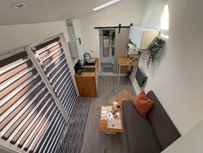 Kompakti oleskelutila, jossa on pieni keittiönurkkaus, sohva, sohvapöytä ja näkymä liukuoven läpi.