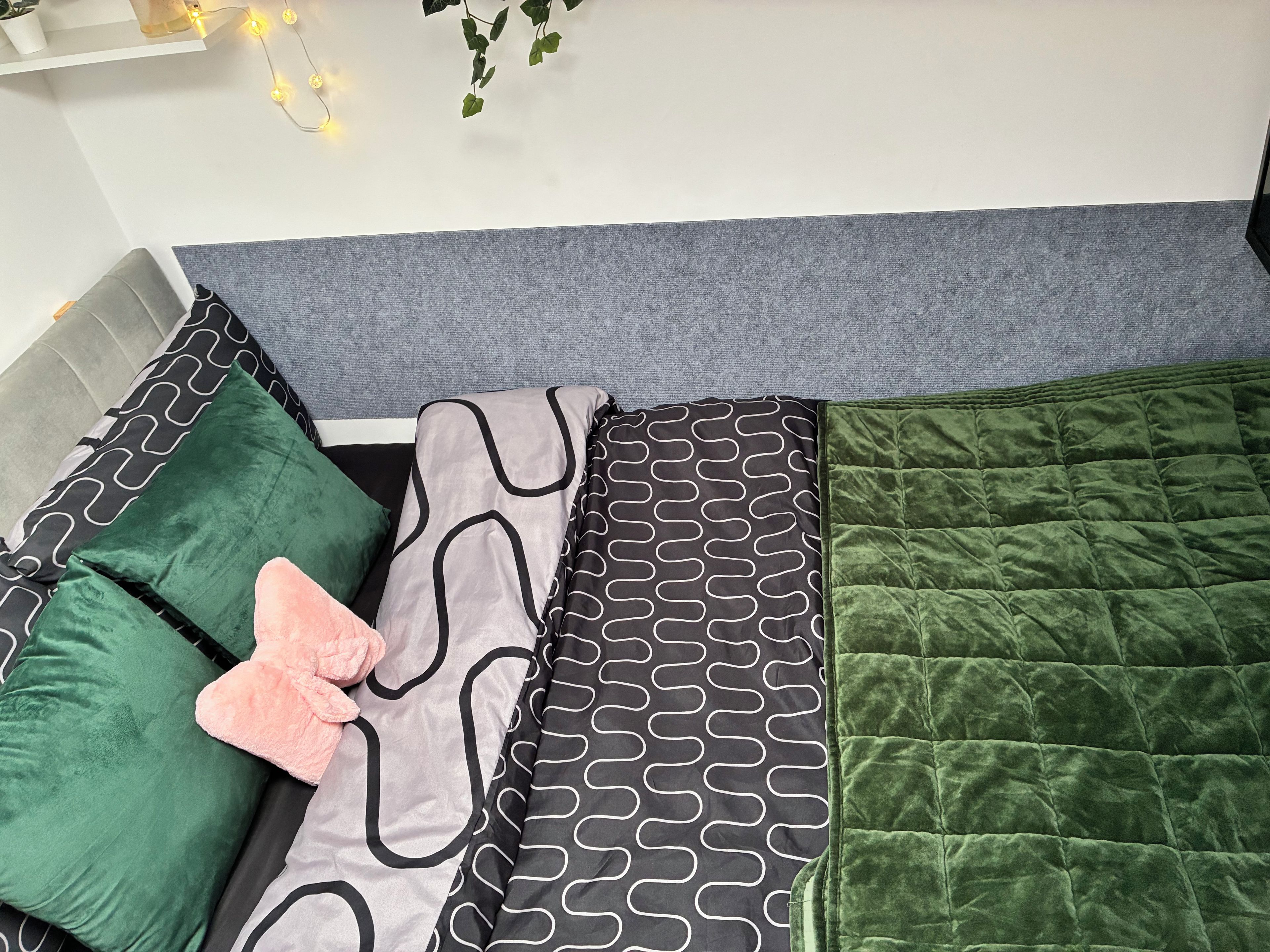Una cama con cabecera gris, pared gris y colcha verde.