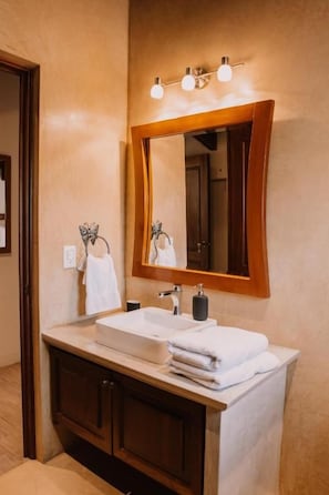 A bathroom with a wooden vanity, a white sink, a mirror with a wooden frame, and a towel rack. - Bärehuus Boutique Hotel (Antigua Guatemala)