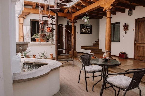 A rustic interior with a stone fountain, wicker chairs, and a staircase leading to an upper level. - Bärehuus Boutique Hotel (Antigua Guatemala)