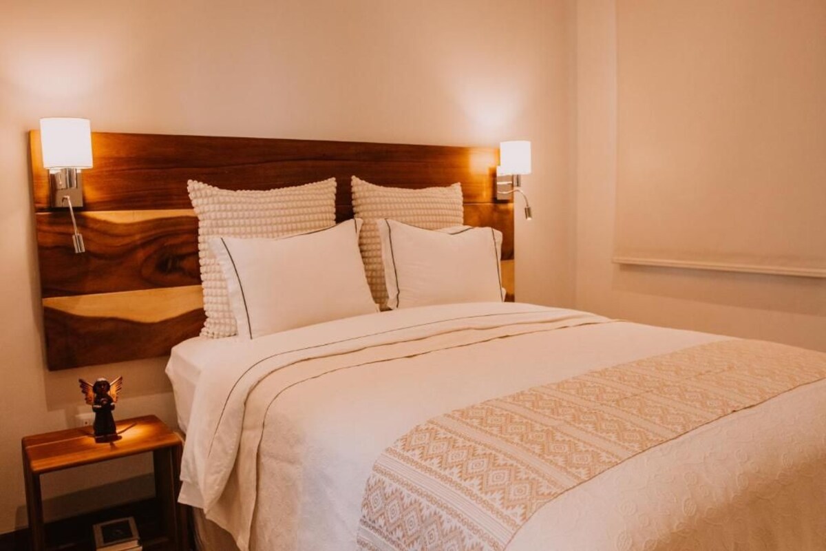 A neatly made bed with a wooden headboard, two bedside lamps, and a small nightstand with a figurine.