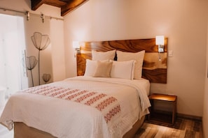 A bedroom with a wooden headboard, a bed with white bedding, a bedside table, and a wall-mounted lamp. - Bärehuus Boutique Hotel (Antigua Guatemala)
