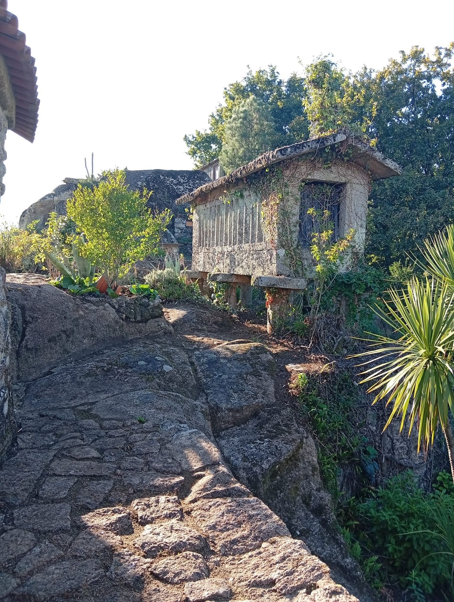 Un bâtiment rustique en pierre, doté d’un toit en pente, entouré de verdure et situé dans un environnement rocheux.