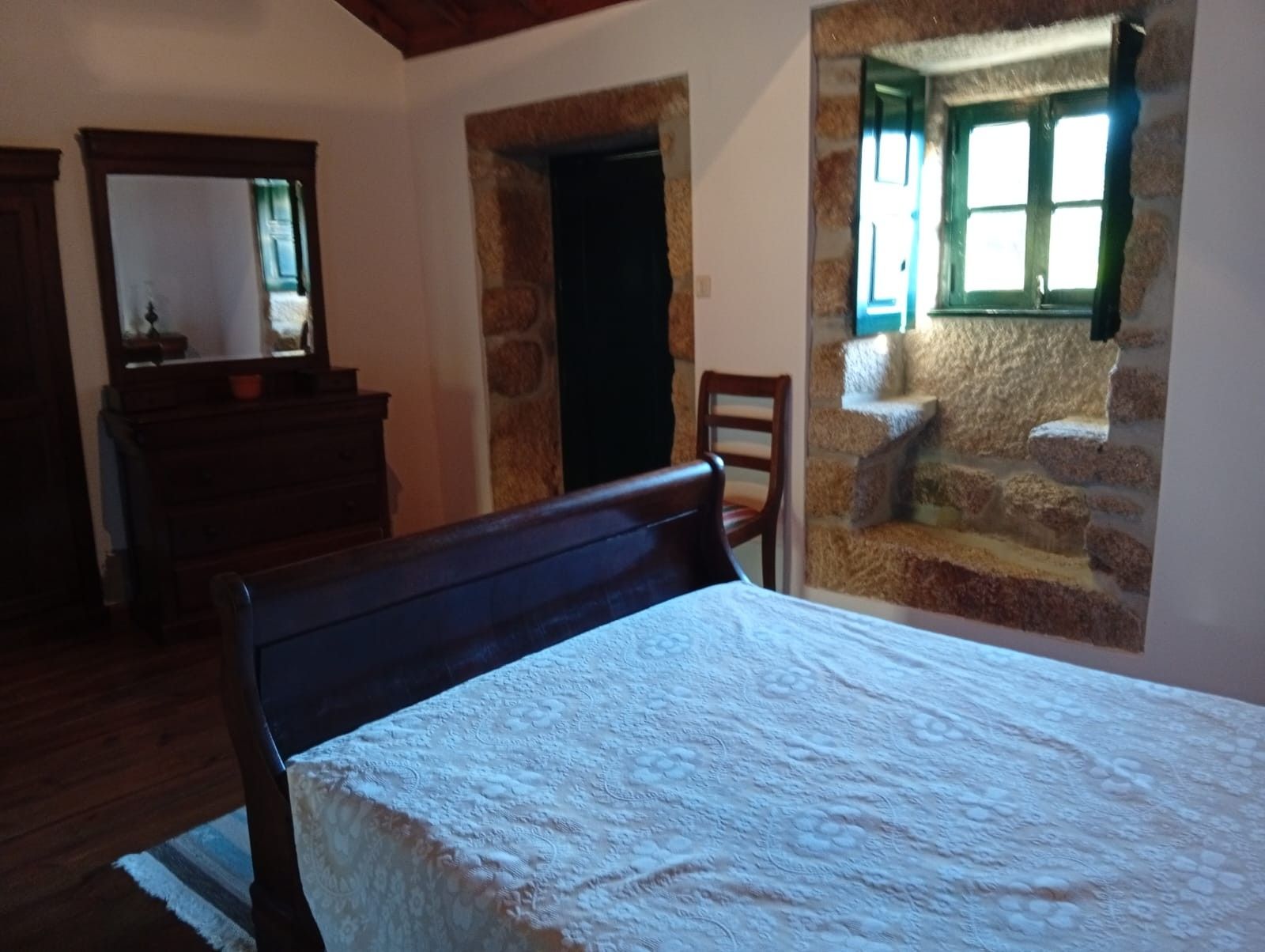 Een slaapkamer met een bed, een kaptafel, een spiegel en een stenen muur met een raam.