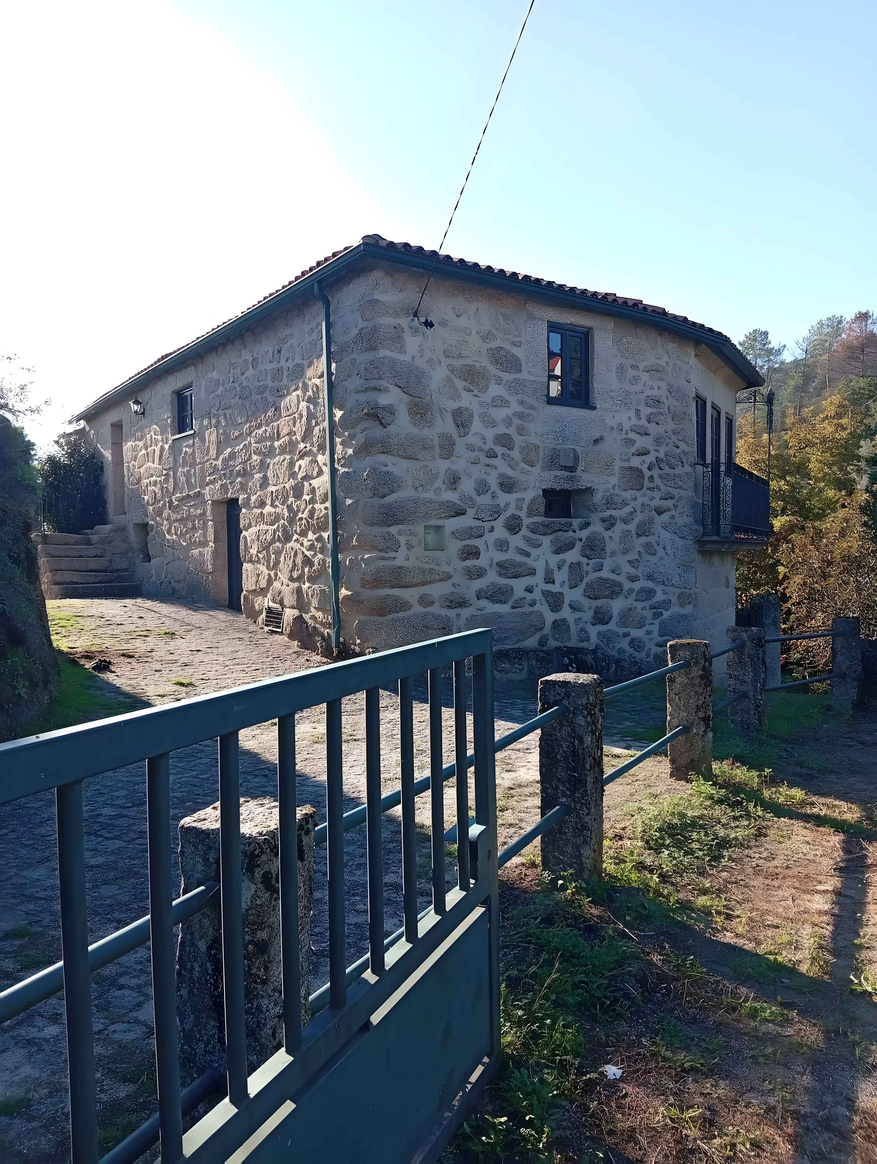 Un bâtiment en pierre doté d’un balcon, d’une petite fenêtre et d’un portail en métal, le tout visible au premier plan.