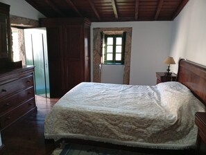 Een slaapkamer met een bed, een houten dressoir en een raam met uitzicht.