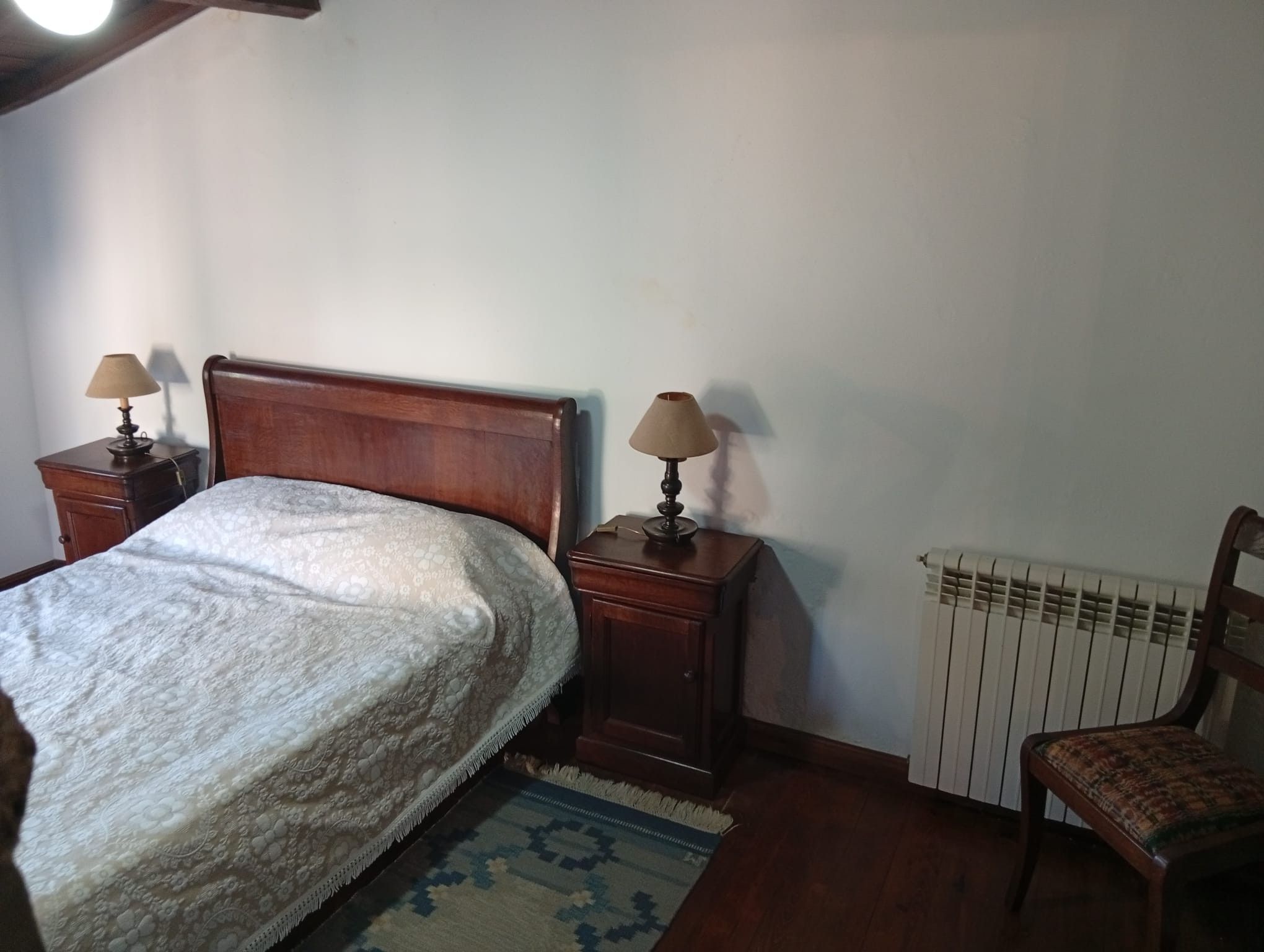 Ein Schlafzimmer mit einem hölzernen Bett, zwei Nachttischen mit Lampen, einem Heizkörper und einem Sessel.
