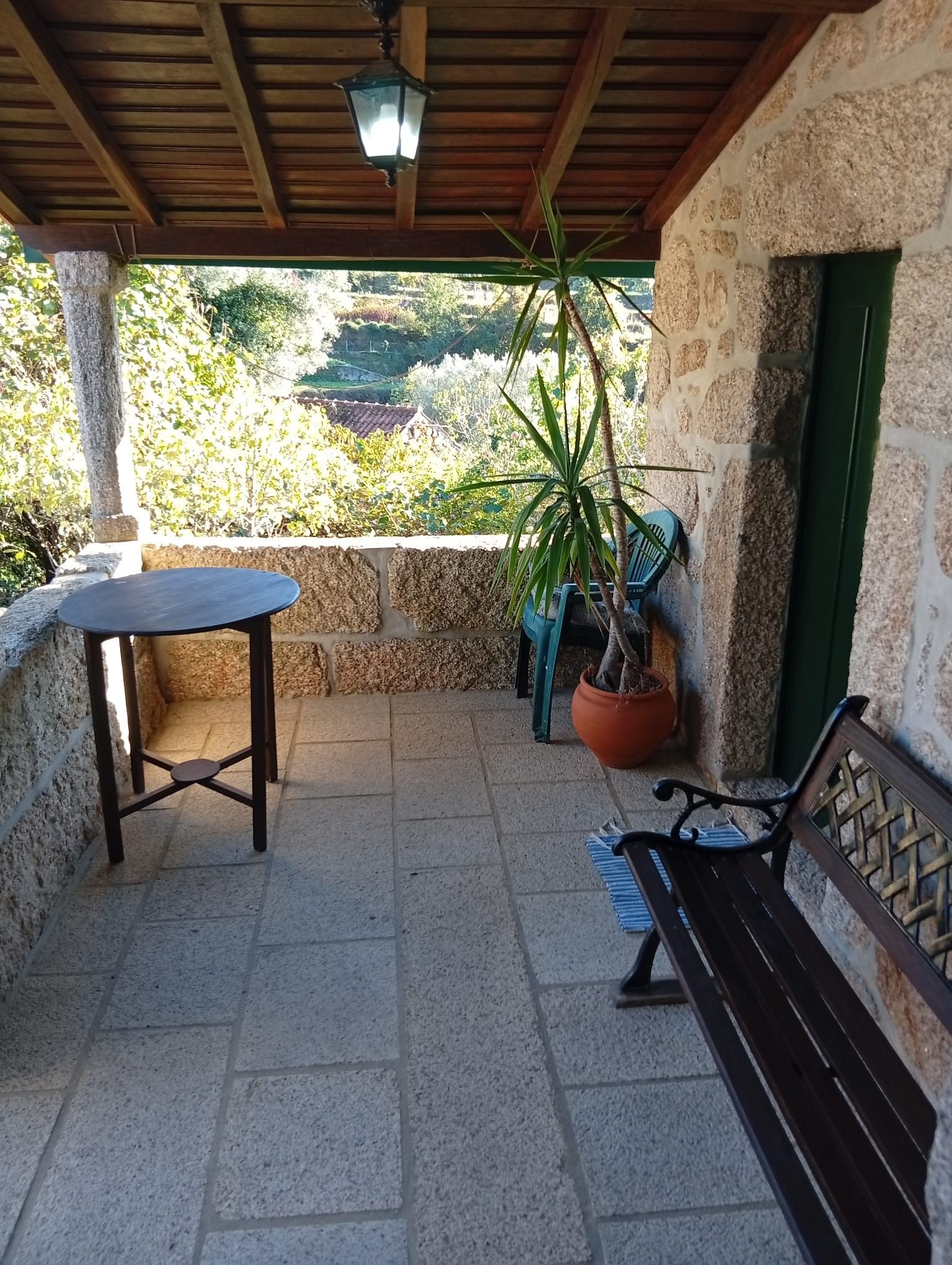 Un espace extérieur abrité, doté d’un mur en pierre, d’une plante en pot, d’une table et d’un banc.