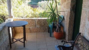Un espace extérieur abrité, doté d’un mur en pierre, d’une plante en pot, d’une table et d’un banc.
