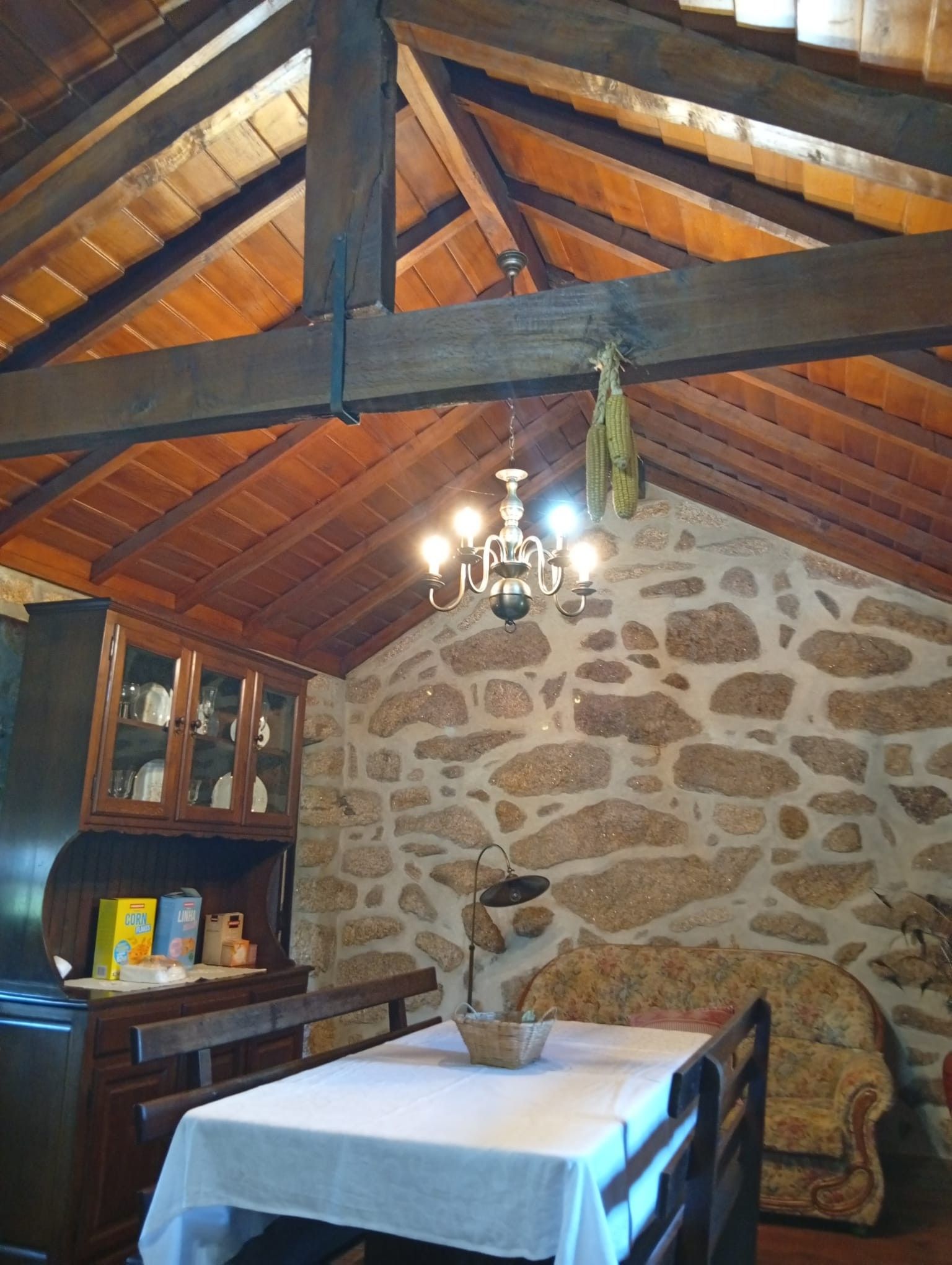 A rustic interior with a stone wall, wooden beams, a chandelier, and a table set for dining.
