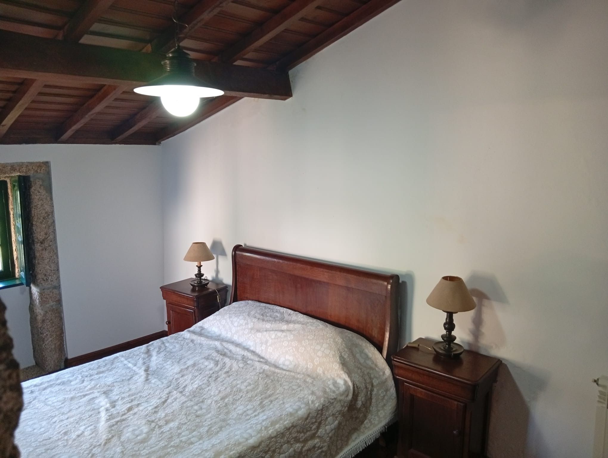 Une chambre avec une tête de lit en bois, deux tables de chevet avec des lampes, un lit recouvert d’une couverture blanche et un plafond en bois.