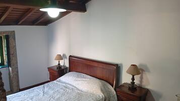 Une chambre avec une tête de lit en bois, deux tables de chevet avec des lampes, un lit recouvert d’une couverture blanche et un plafond en bois.