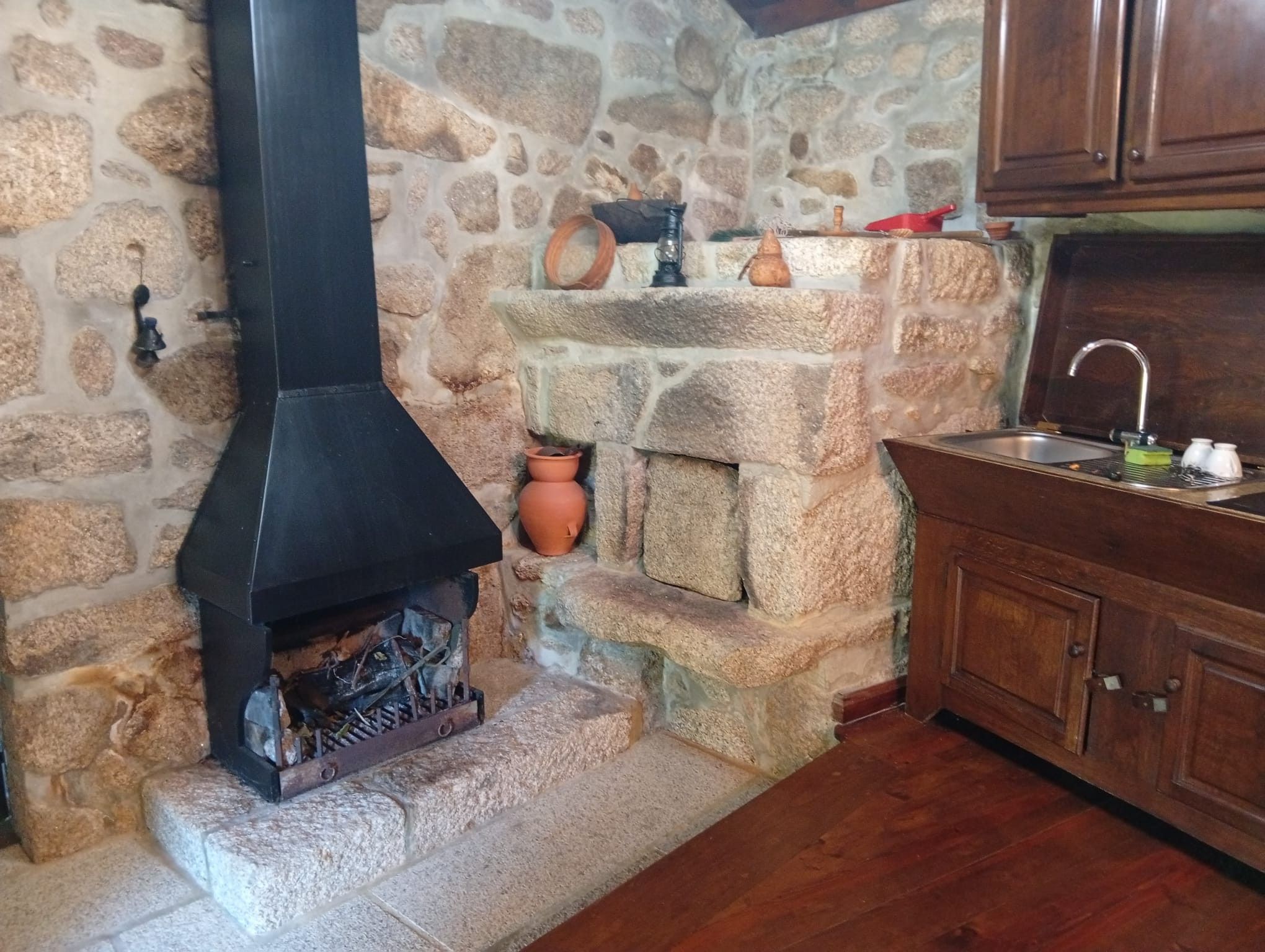 Une cheminée en pierre avec une cheminée noire, une cuisine rustique avec des armoires en bois et un mur en pierre.