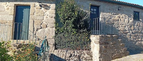A stone building with two windows, a metal gate, and a small garden area.
