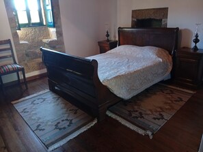 A bedroom with a wooden bed, a nightstand, a chair, and a stone wall. - Room 'Suite 1' with Mountain View, Shared Garden and Wi-Fi (Soajo)