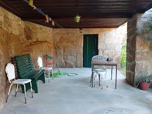 Zona d'estar a l'aire lliure coberta, amb parets de pedra, sostre de fusta i una porta verda.