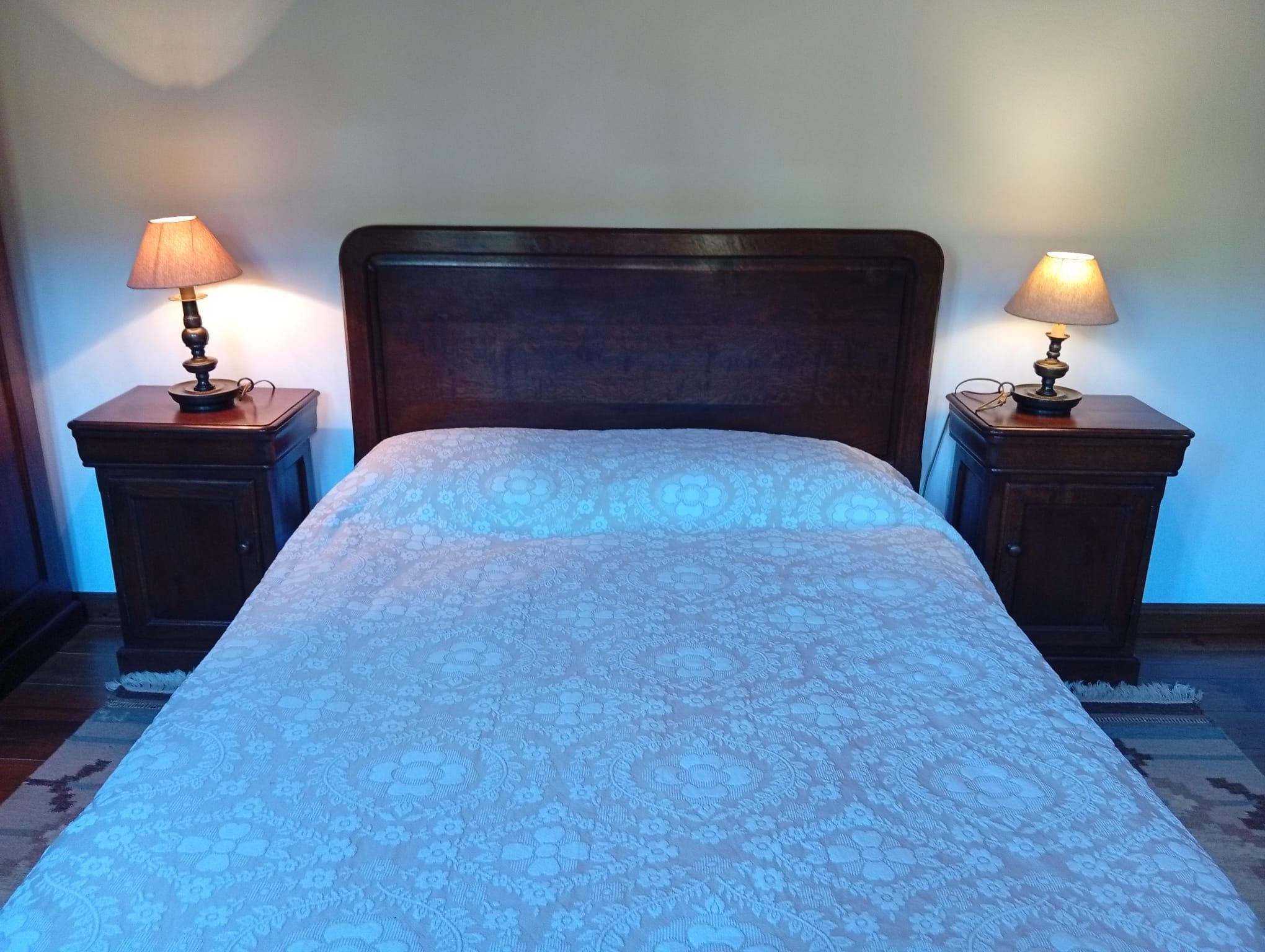 A bed with a floral patterned bedspread, flanked by two nightstands with lamps, in a room with a wooden headboard.