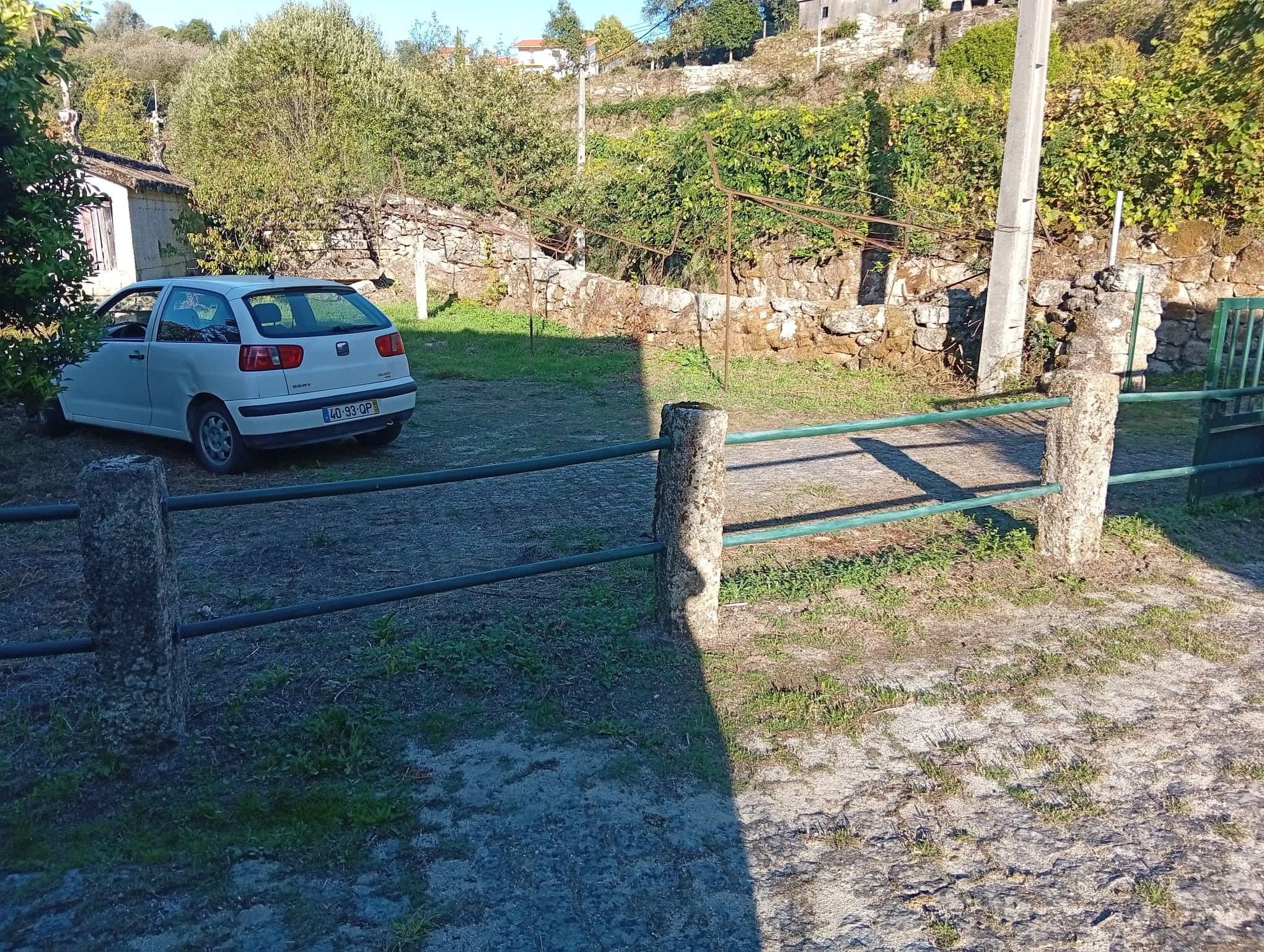 Une voiture blanche est garée dans une allée, avec un mur de pierres et de la verdure en arrière-plan.