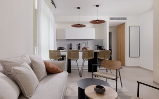 A modern living room with a sofa, chairs, a coffee table, and a kitchen in the background.