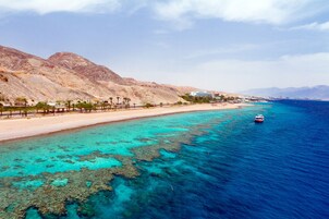 A coastal area with clear turquoise waters, a sandy beach, and a mountainous backdrop.