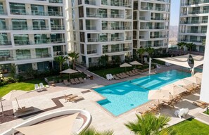 Un hotel moderno con piscina en la azotea, varios balcones y zonas de estar al aire libre.