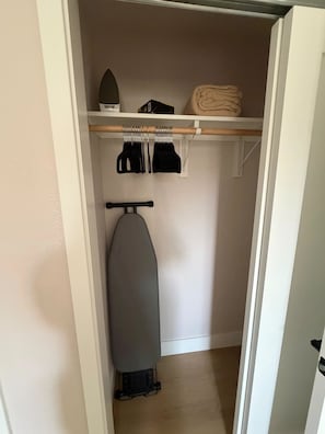 A closet with hanging clothes, a shelf with folded items, and an ironing board. - Brand-New Renovated 4BR/2BA l Prime Hayward Location (Hayward)