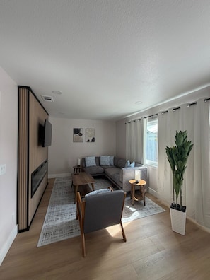 Ein modernes Wohnzimmer mit einem Ecksofa, einem Holz-TV-Möbel, einem Esstisch und einer Topfpflanze.