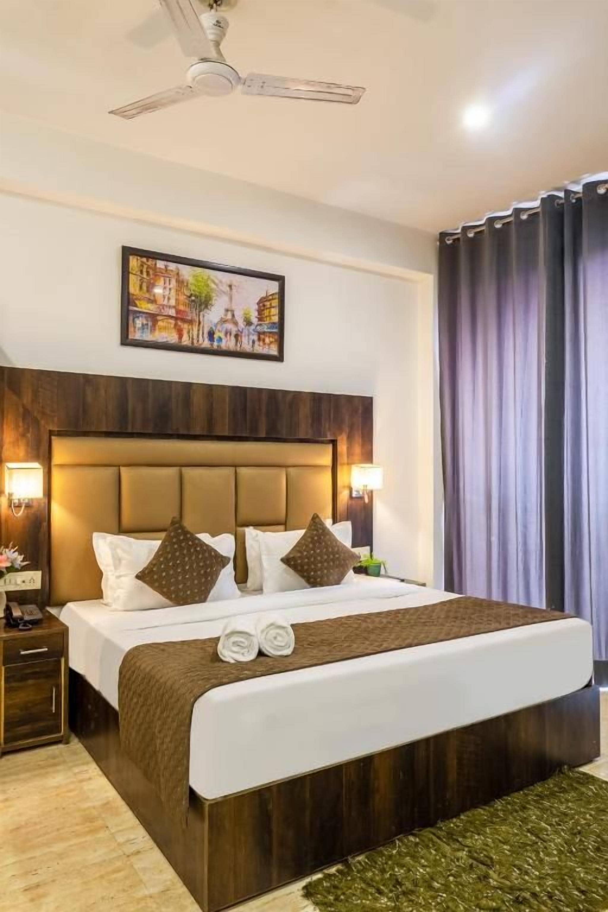 A hotel room with a large bed, a headboard with a picture, bedside lamps, and a ceiling fan.