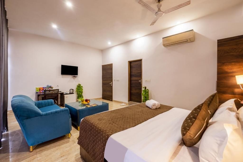 Una habitación de hotel con cama, un sillón azul, una mesita, televisor y aire acondicionado.
