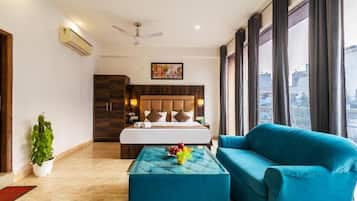 A hotel room with a bed, a blue sofa, a glass coffee table with fruit, a potted plant, and a city view.