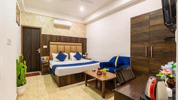 Quarto de hotel com cama, sofá, escrivaninha, televisão e guarda-roupa.
