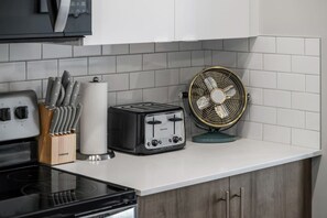A kitchen with a stove, a toaster, a fan, and a knife block. - `Auburn` 1 King  1 Queen Bed | UG Parking | Sofa Bed (Calgary)
