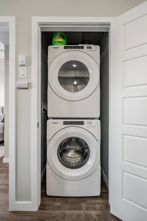 Un lavadero con dos lavadoras Whirlpool apiladas, una botella verde de detergente y una puerta blanca.