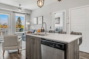 A modern kitchen with a central island, built-in dishwasher, and a ceiling fan. - `Auburn` 1 King  1 Queen Bed | UG Parking | Sofa Bed (Calgary)
