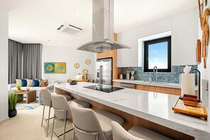 Een moderne keuken met een centraal eiland, barkrukken, een koelkast en een raam.
