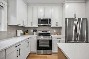 A modern kitchen with white cabinetry, stainless steel appliances, and a marble countertop. - The Evergreen | 3 Bed | Garage | Min to Hospital (Calgary)