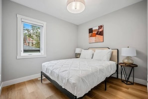 A bedroom with a bed, a nightstand, a lamp, a window, and a painting on the wall. - The Evergreen | 3 Bed | Garage | Min to Hospital (Calgary)