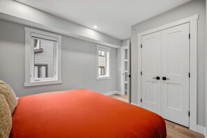 Ein Schlafzimmer mit einem Bett, zwei Fenstern, einem Kleiderschrank und einer Tür.
