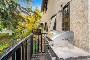 A barbecue grill on a balcony with a view of trees and a house. - The Woodside | 2 King | Foosball | Pull out Couch (Calgary)