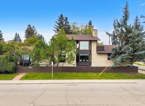 A modern two-story house with a flat roof, a visible garage, and a well-maintained lawn. - The Woodside | 2 King | Foosball | Pull out Couch (Calgary)