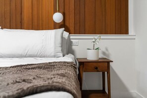 A bedroom with a bed, a bedside table with a plant, and a wall-mounted light fixture. - The Woodside | 2 King | Foosball | Pull out Couch (Calgary)